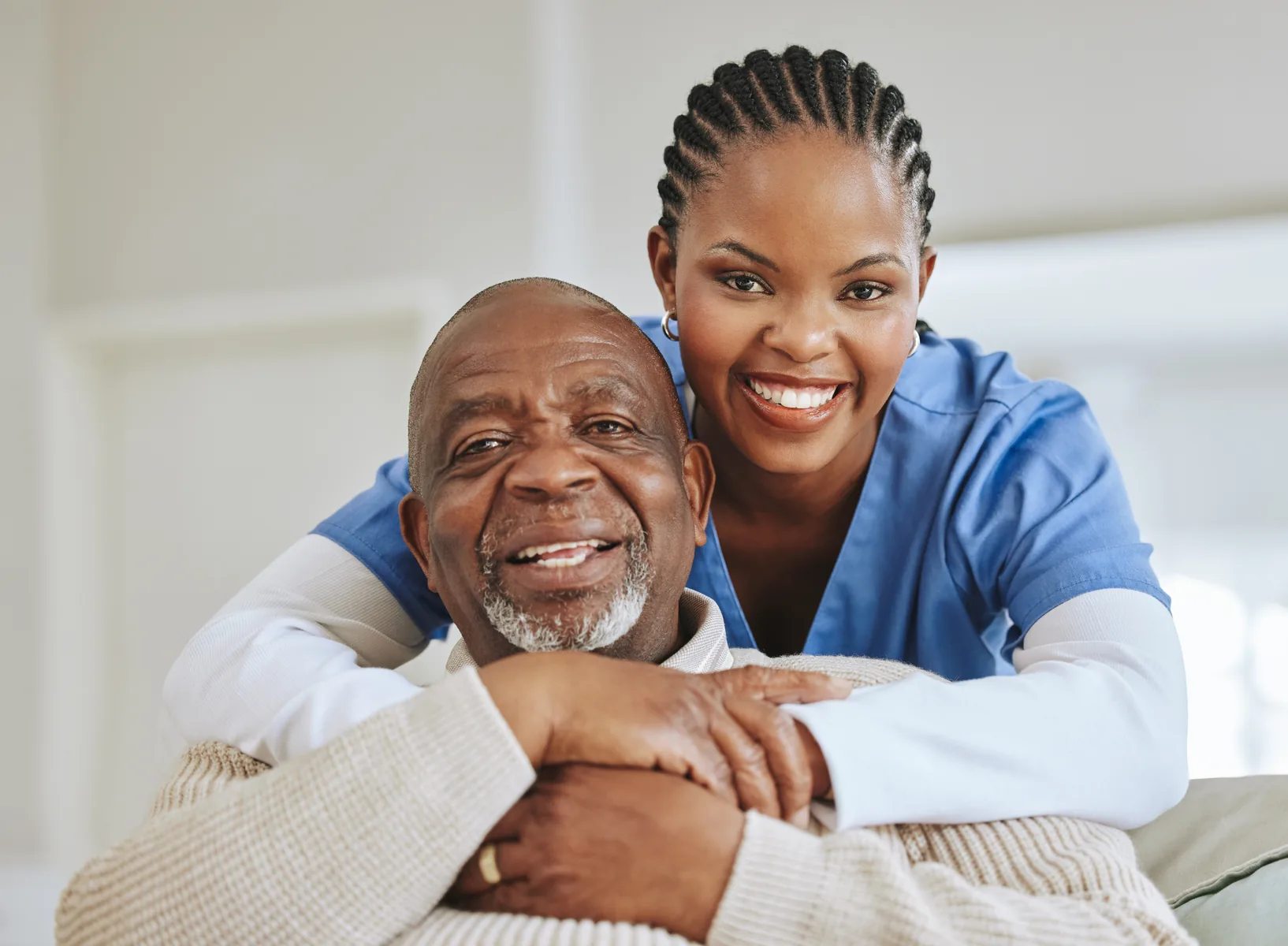 A smiling woman in blue scrubs embracing an older man.
