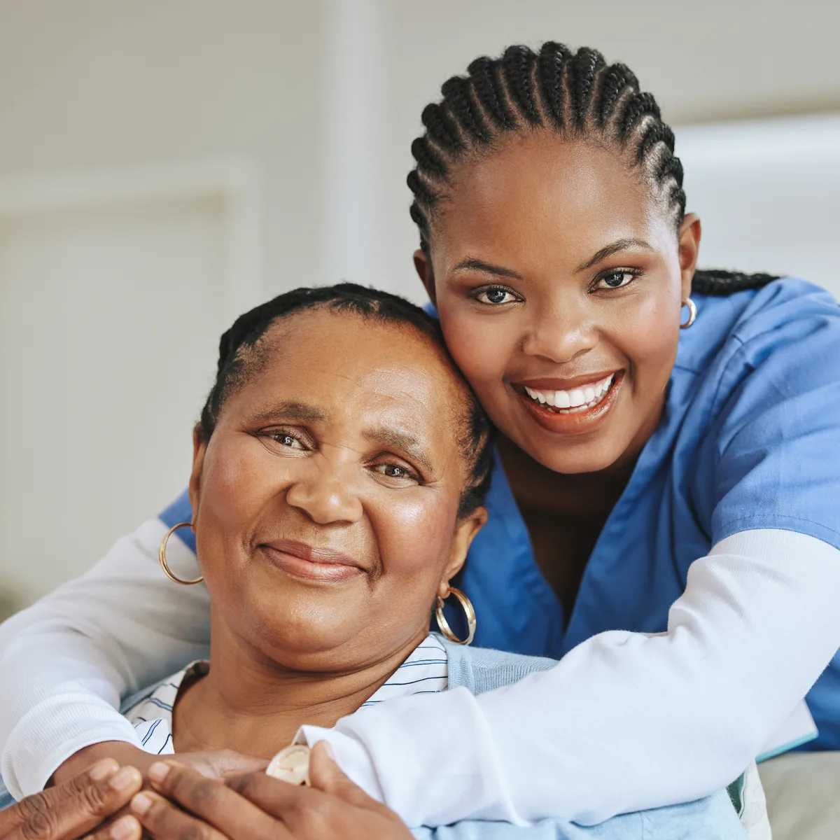 An older woman and a woman in blue scrubs sharing an embrace.