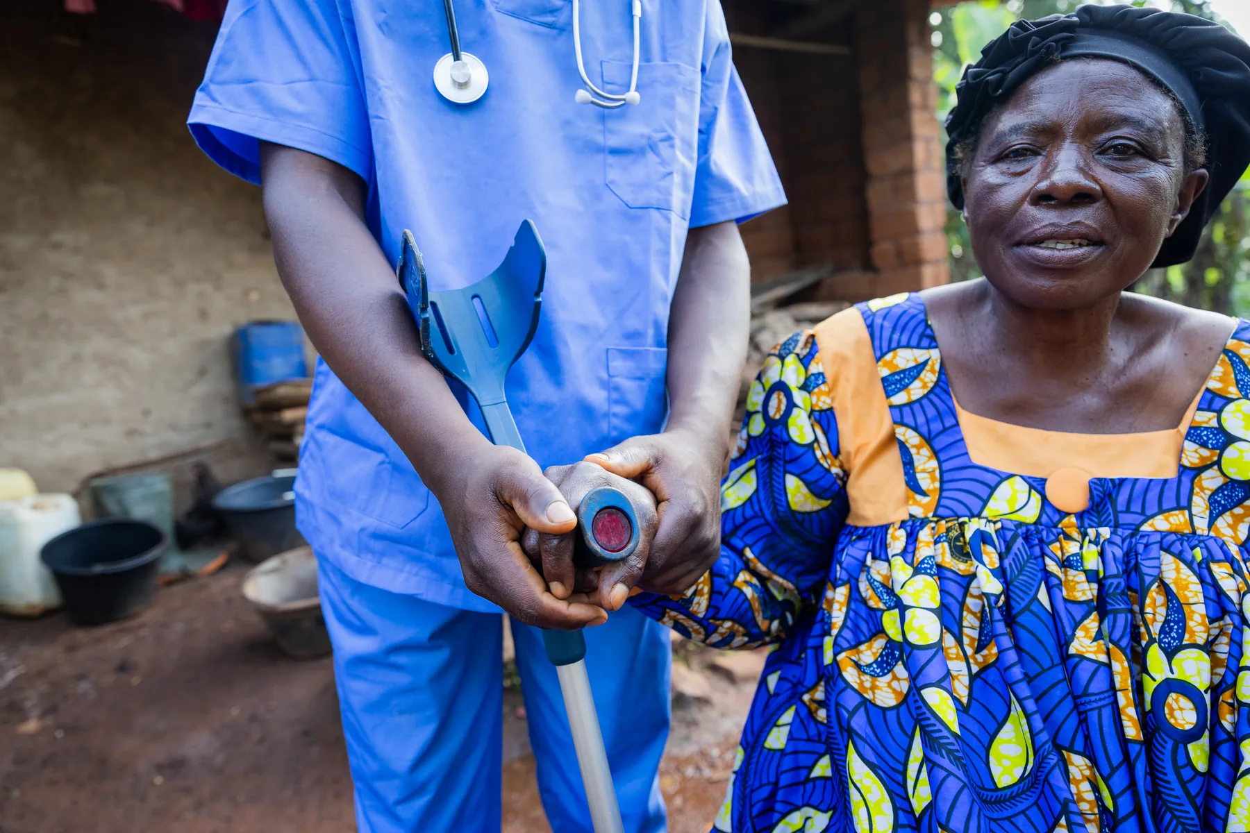A person in blue scrubs holding a small device beside an older woman.